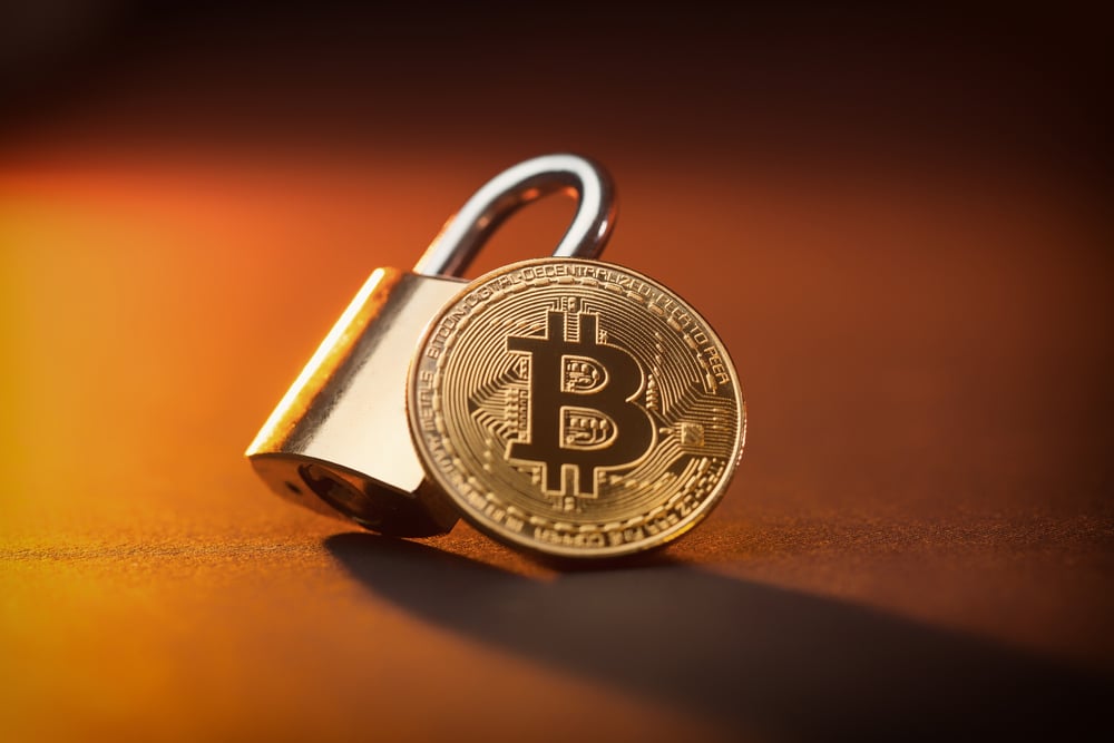 Moeda de ouro com o logótipo Bitcoin apoiado sobre um cadeado. Representa uma moeda criptográfica segura.