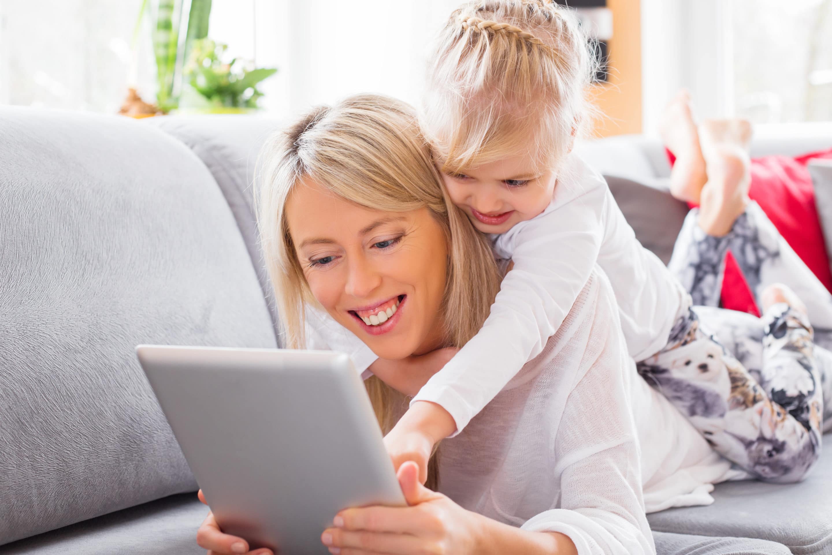Madre e hijo sonríen mientras utilizan un iPad protegido por una VPN. La VPN mantiene su iPad seguro y protegido.
