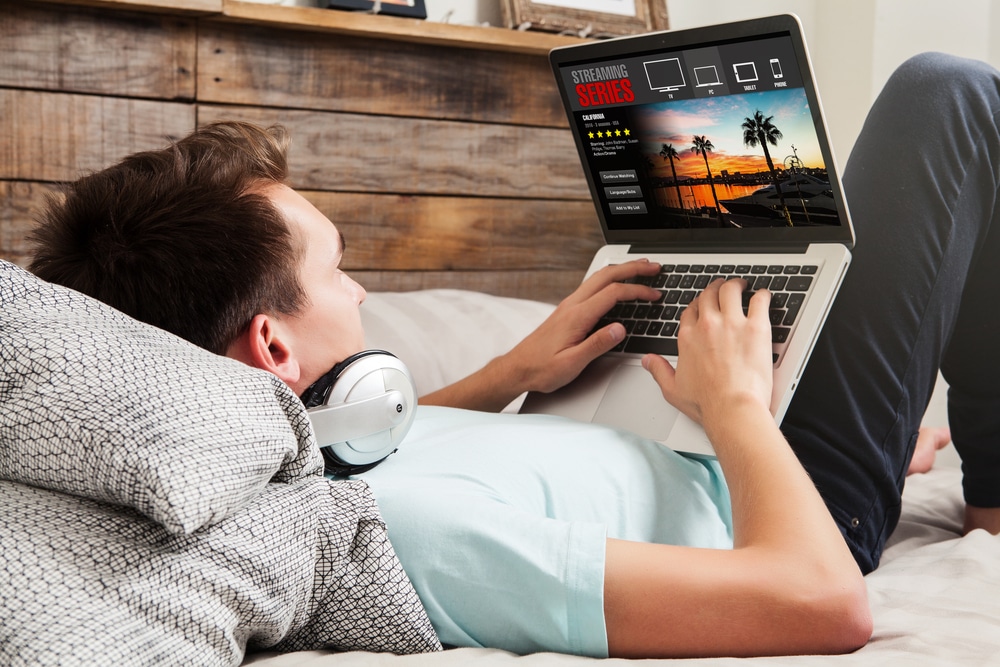 Young adult male streaming movies with a VPN on a laptop in bed.